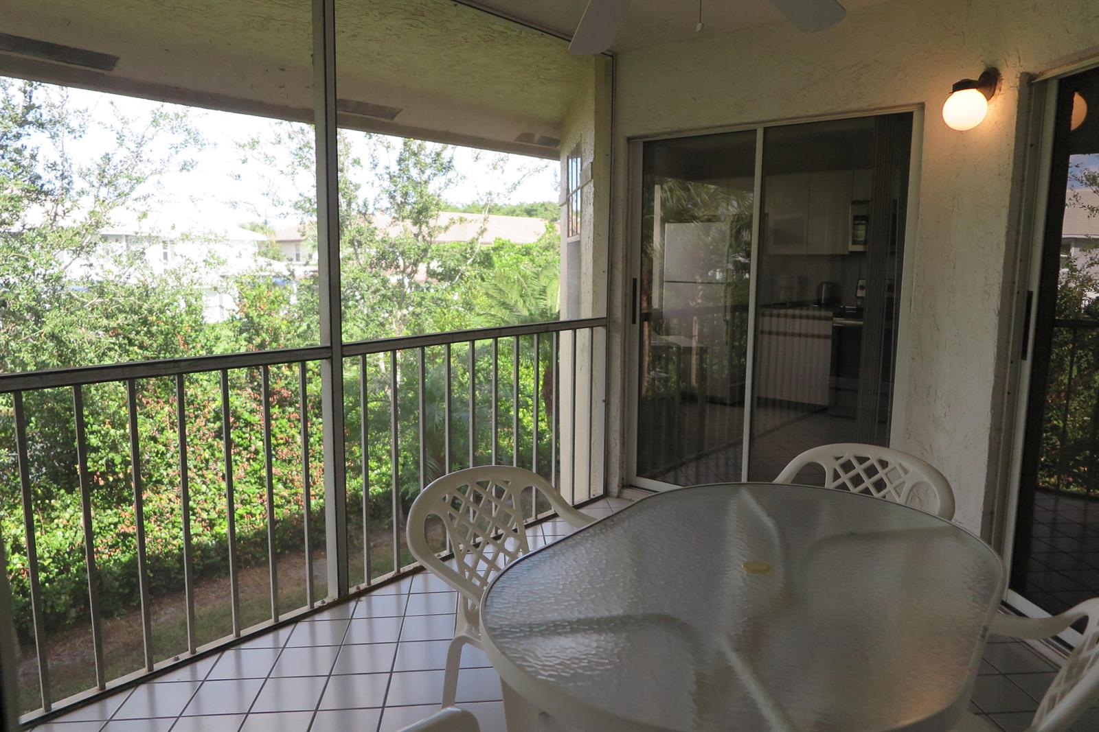 A screened-in balcony with a glass-top table, white chairs, and a view of trees — 6707 Via Regina, Boca Raton FL 33433, BOCA RATON, FL