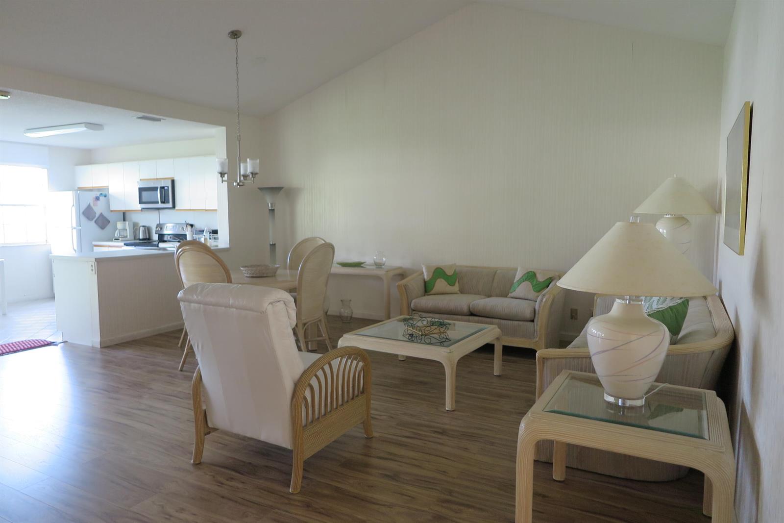 A living room with light-colored furniture, wood-look flooring, and an adjacent open kitchen — 6707 Via Regina, Boca Raton FL 33433, BOCA RATON, FL