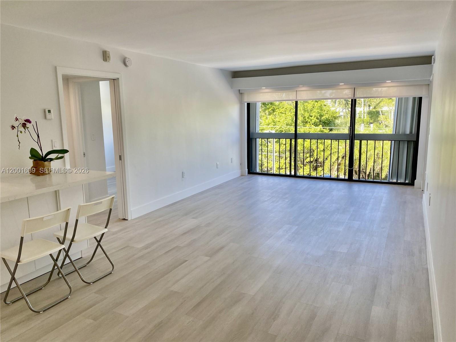 An empty living room features light wood-look flooring, white walls, and a large sliding glass door — 255 Galen Dr # 3D, Key Biscayne FL 33149, KEY BISCAYNE, FL
