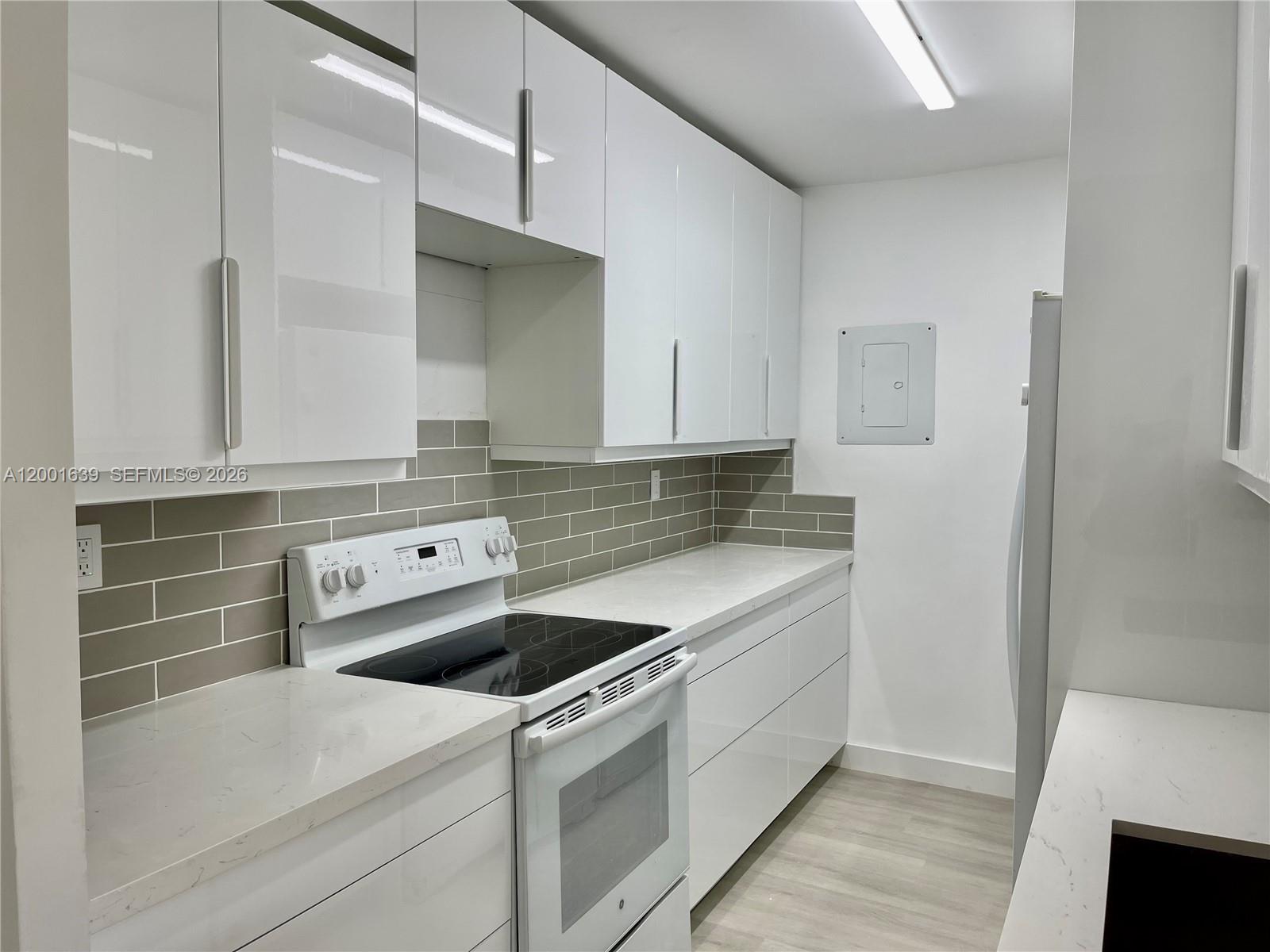 A modern kitchen features white glossy cabinets, a glass-top stove, and gray subway tile backsplash — 255 Galen Dr # 3D, Key Biscayne FL 33149, KEY BISCAYNE, FL