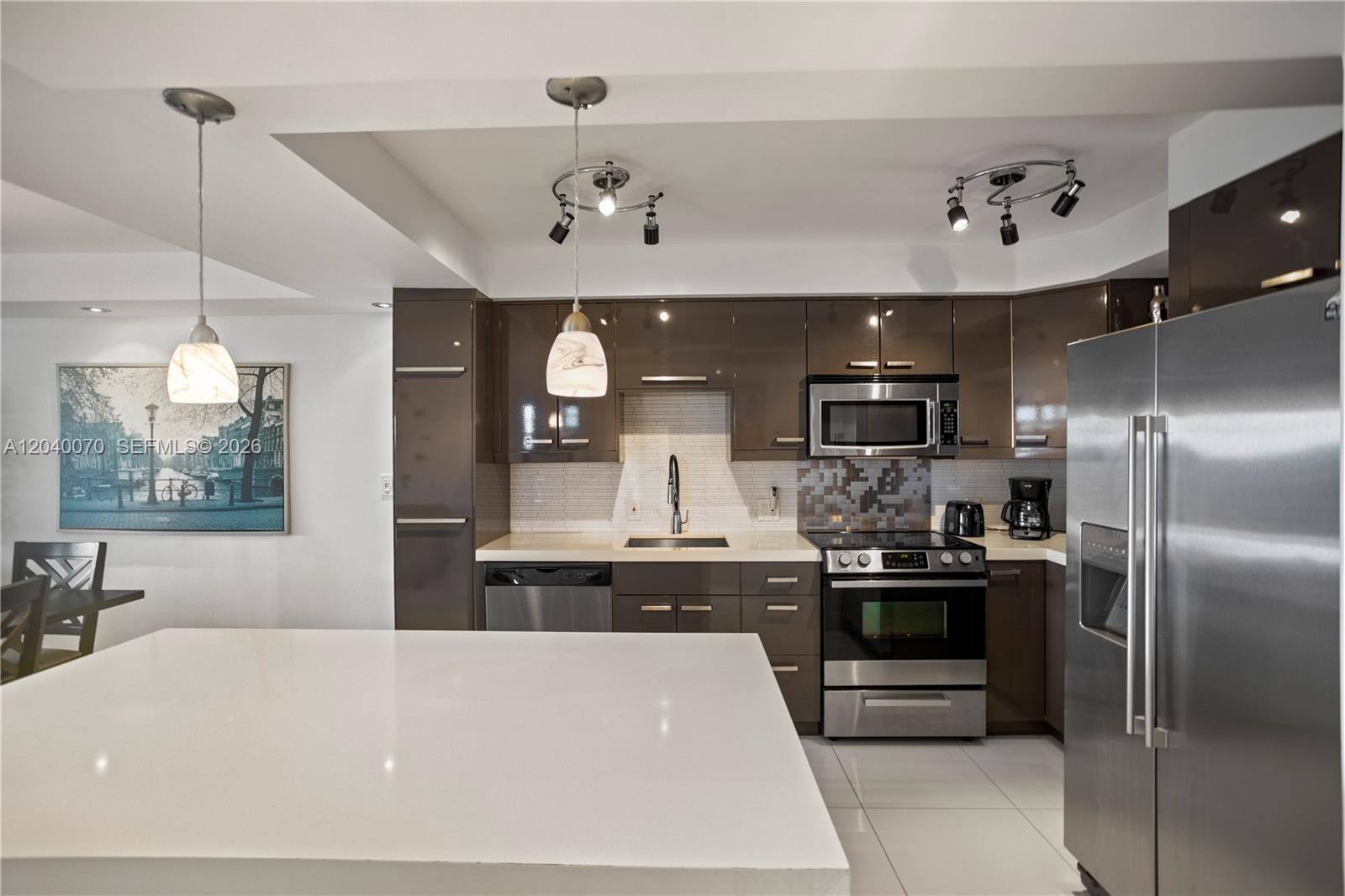 A modern kitchen features glossy brown cabinets, stainless steel appliances, and a white island countertop — 3050 N Palm Aire Dr # 710, Pompano Beach FL 33069, POMPANO BEACH, FL