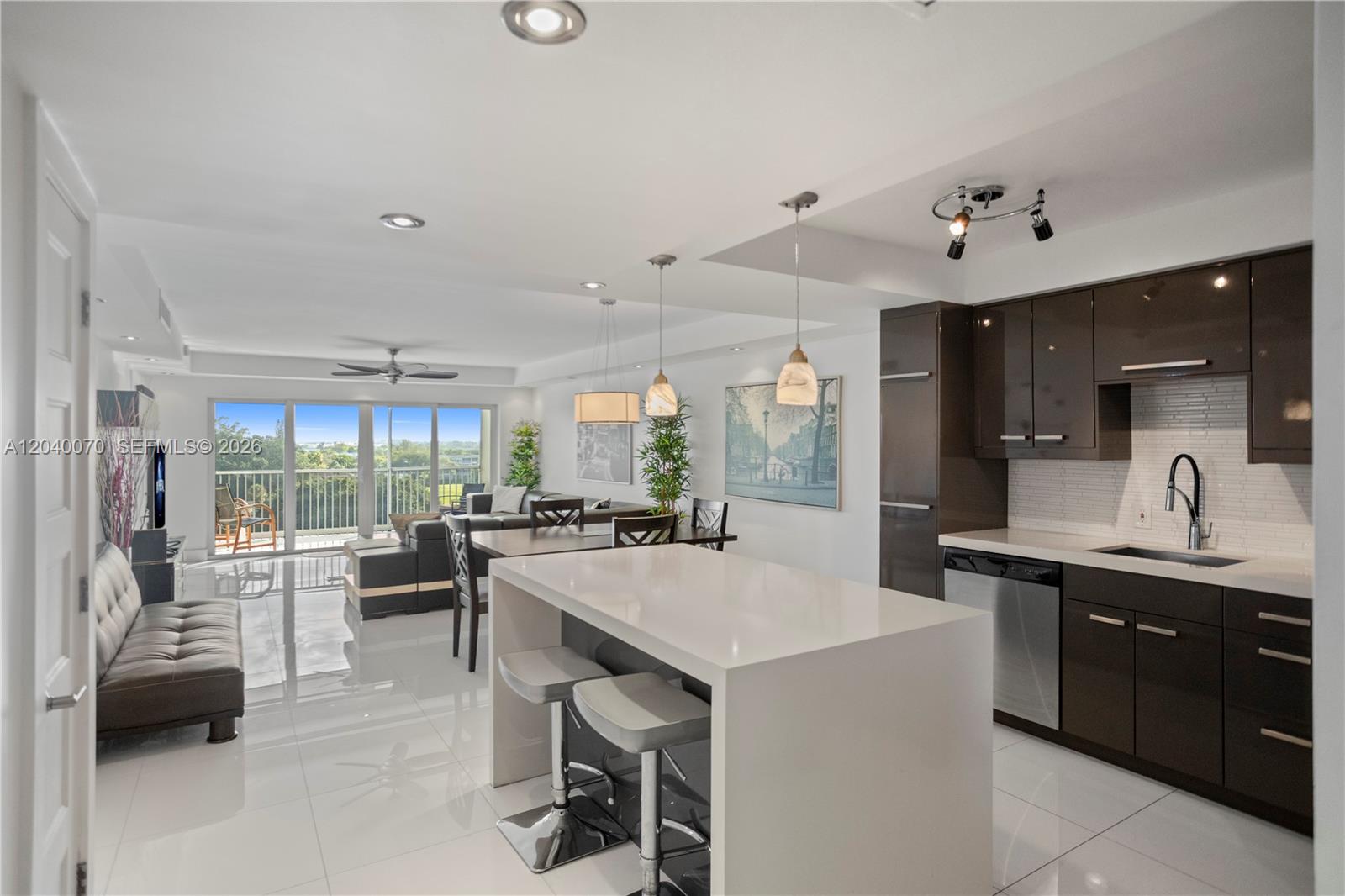 A modern kitchen with dark cabinetry and a white island opens into a bright living area — 3050 N Palm Aire Dr # 710, Pompano Beach FL 33069, POMPANO BEACH, FL