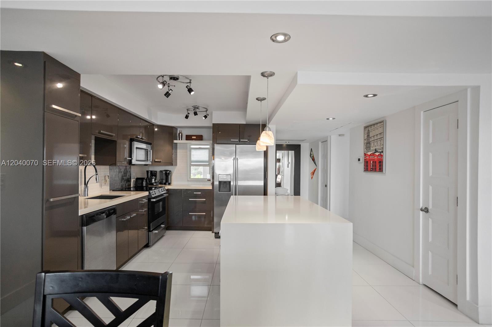 A modern kitchen features glossy brown cabinets, white countertops, and a large central island — 3050 N Palm Aire Dr # 710, Pompano Beach FL 33069, POMPANO BEACH, FL