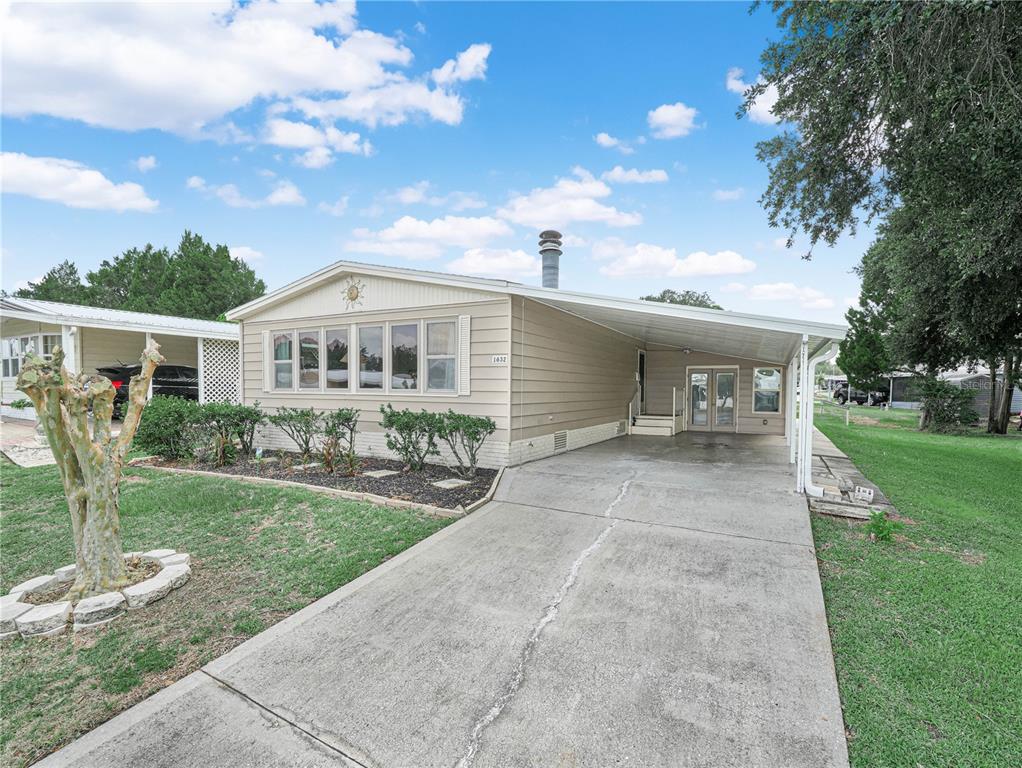 A single-story mobile home with tan siding, a concrete driveway, and a covered carport — 1632 FOXWAY DRIVE, LAKELAND, FL