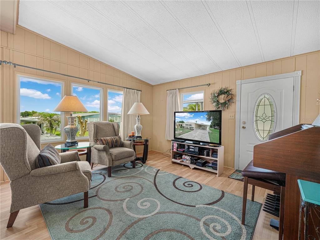 A living room features light wood walls, a patterned rug, two armchairs, and a television — 1632 FOXWAY DRIVE, LAKELAND, FL