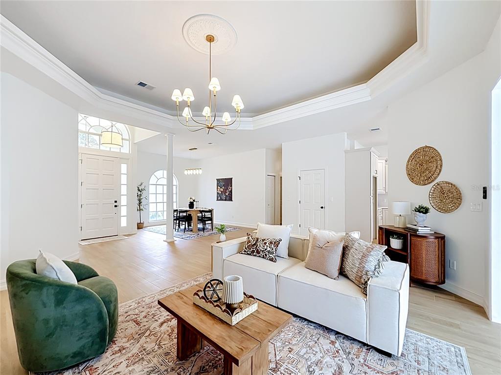 A bright living room features a white sofa, green armchair, wooden coffee table, and chandelier — 34239 WOODRIDGE LANE, EUSTIS, FL