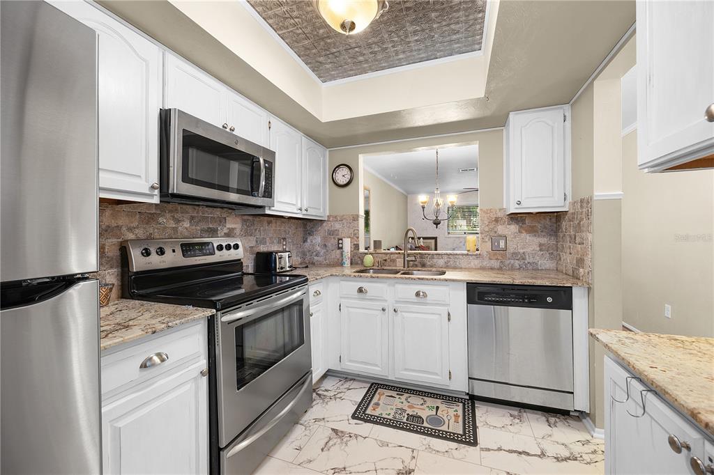 A kitchen features white cabinets, stainless steel appliances, granite countertops, and a tiled floor — 1001 PINE ISLE LANE UNIT 1001, NAPLES, FL