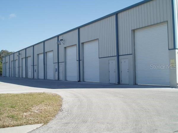 A long industrial warehouse building features multiple roll-up garage doors and adjacent pedestrian entry doors — 140 OSCAR HILL ROAD, TARPON SPRINGS, FL