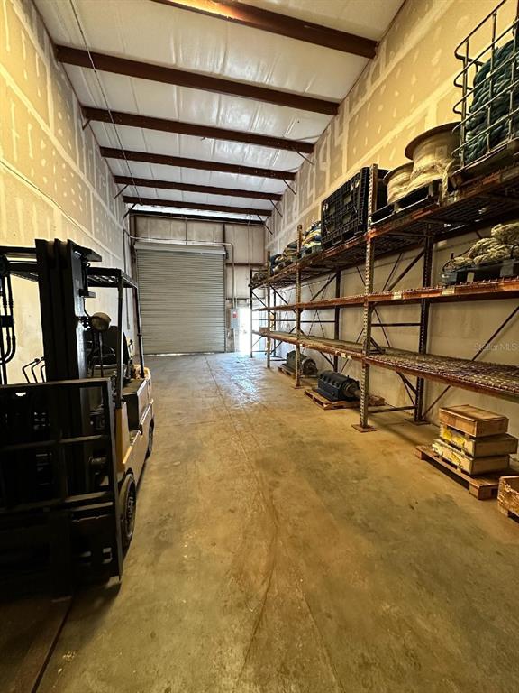 A warehouse interior features a forklift, metal storage shelving, and a large roll-up garage door — 140 OSCAR HILL ROAD, TARPON SPRINGS, FL