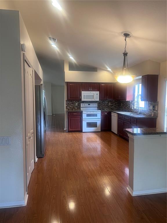 A kitchen features dark wood cabinets, granite countertops, a tiled backsplash, and hardwood flooring — 924 RIDGE HAVEN DRIVE, BRANDON, FL