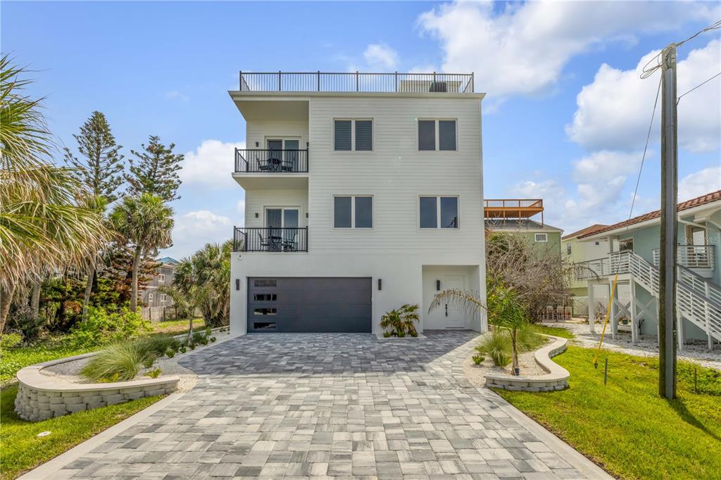 A three-story white house with a paved driveway, a garage, and balconies on the left — 6857 TURTLEMOUND ROAD, NEW SMYRNA BEACH, FL