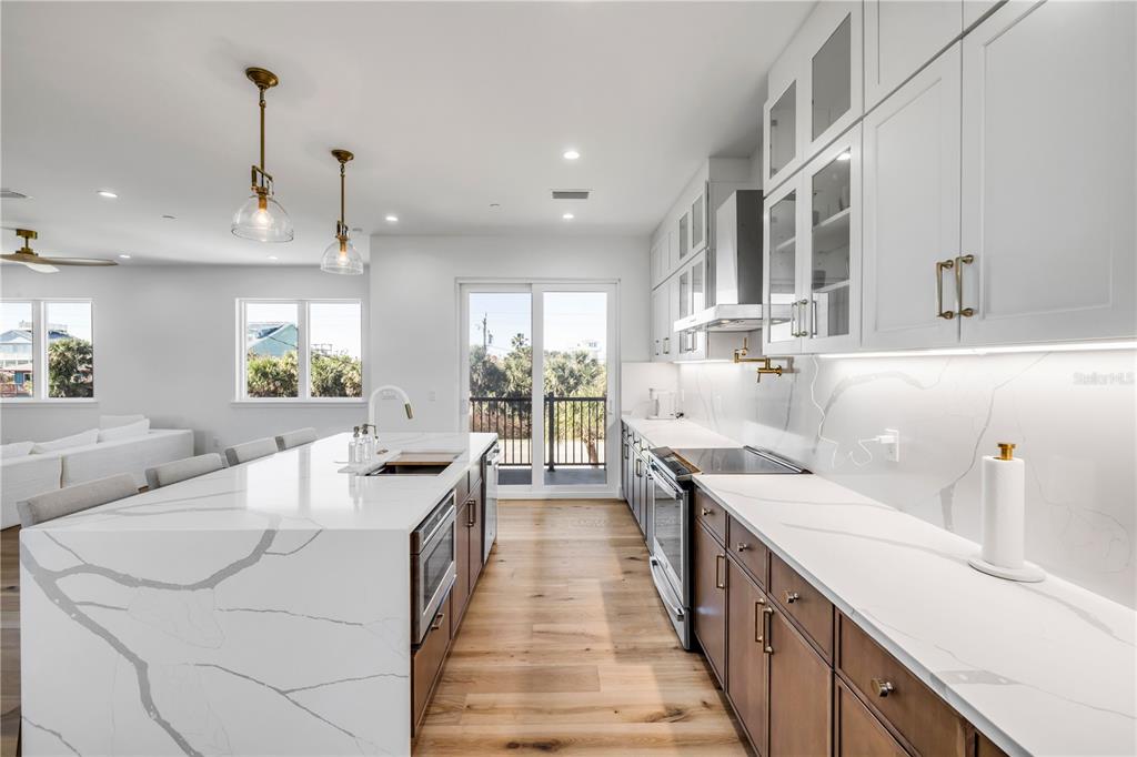 A modern kitchen features a large white marble island, wood cabinets, and stainless steel appliances — 6857 TURTLEMOUND ROAD, NEW SMYRNA BEACH, FL