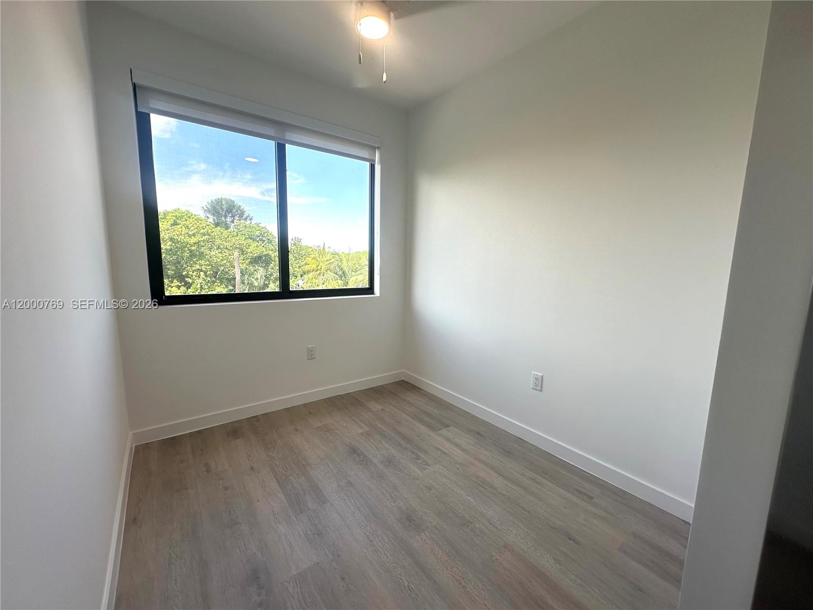 An empty room features white walls, light wood-look flooring, and a large window with views — 20 NE 19th Ave # 304, Pompano Beach FL 33060, POMPANO BEACH, FL