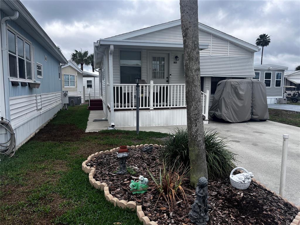 A white manufactured home features a front porch, a covered golf cart, and landscaped mulch — 9000 US HIGHWAY 192 UNIT 317, CLERMONT, FL