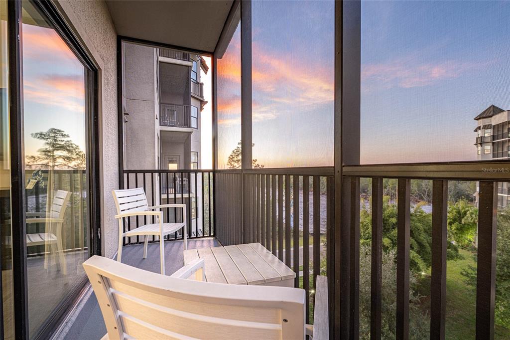 A screened-in balcony features white chairs, a small table, and views of nearby buildings — 14501 GROVE RESORT AVENUE UNIT 2534, WINTER GARDEN, FL