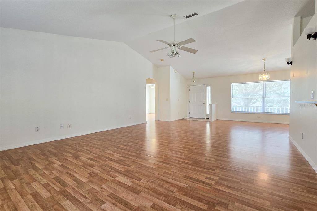 A spacious living room features vaulted ceilings, wood-look flooring, and a ceiling fan — 10417 LAKE HASSON CIRCLE, CLERMONT, FL