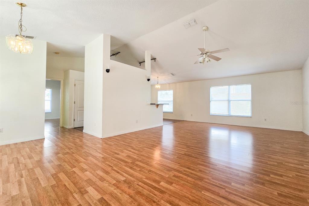 An open-concept living area features vaulted ceilings, wood-look flooring, and a central partition wall — 10417 LAKE HASSON CIRCLE, CLERMONT, FL