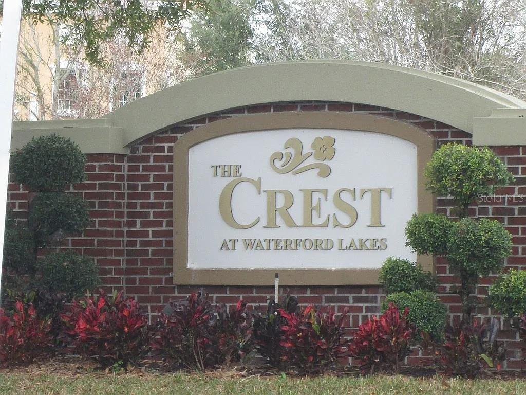 A brick monument sign displays the name The Crest at Waterford Lakes — 12500 CREST SPRINGS LANE UNIT 1027, ORLANDO, FL