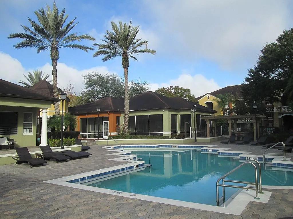 A swimming pool with lounge chairs sits in front of a multi-story apartment complex — 12500 CREST SPRINGS LANE UNIT 1027, ORLANDO, FL