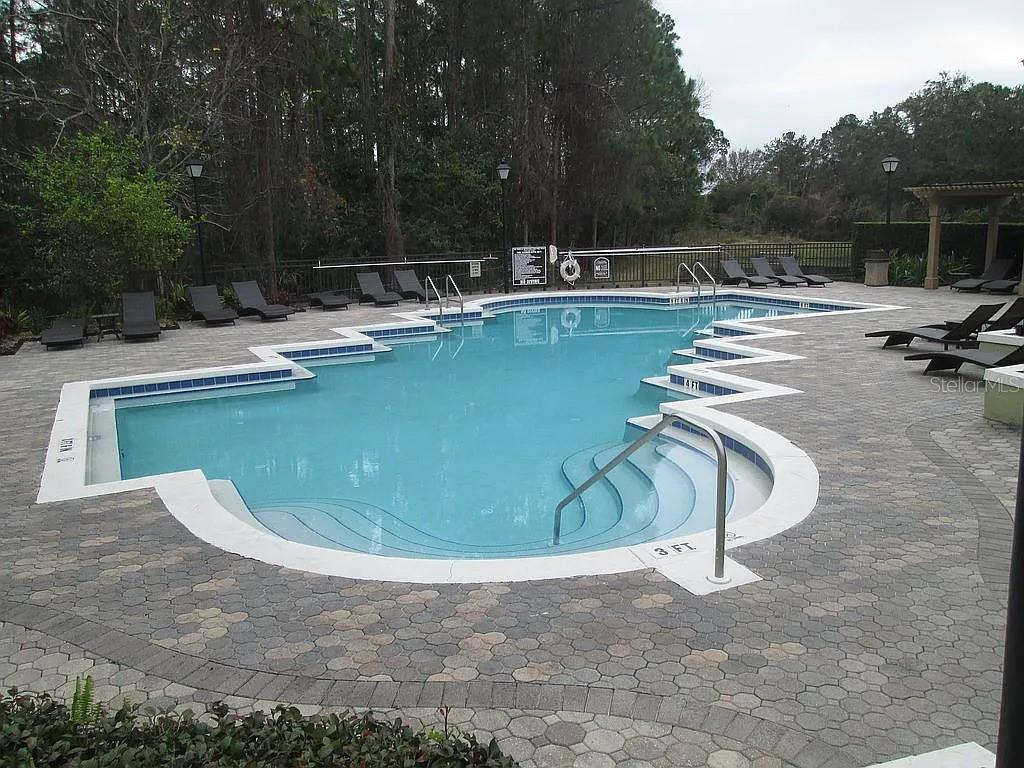 An outdoor swimming pool with a paved deck and lounge chairs surrounded by trees — 12500 CREST SPRINGS LANE UNIT 1027, ORLANDO, FL