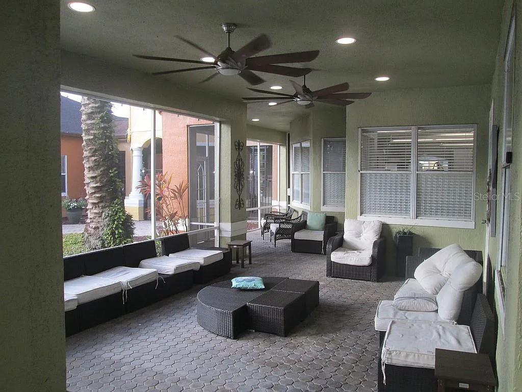 A covered patio features wicker furniture, ceiling fans, and a paver floor overlooking a yard — 12500 CREST SPRINGS LANE UNIT 1027, ORLANDO, FL