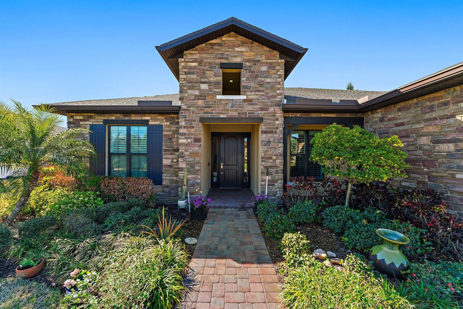 The exterior of a stone-faced house features a brick walkway leading to the front door — 6291 Arcadia Square, Vero Beach FL 32966, VERO BEACH, FL