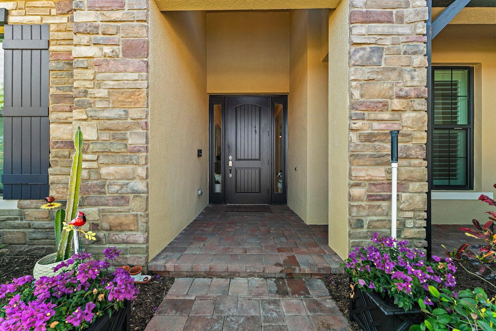 A front entryway features a dark wood door, stone veneer siding, and purple flowering plants — 6291 Arcadia Square, Vero Beach FL 32966, VERO BEACH, FL