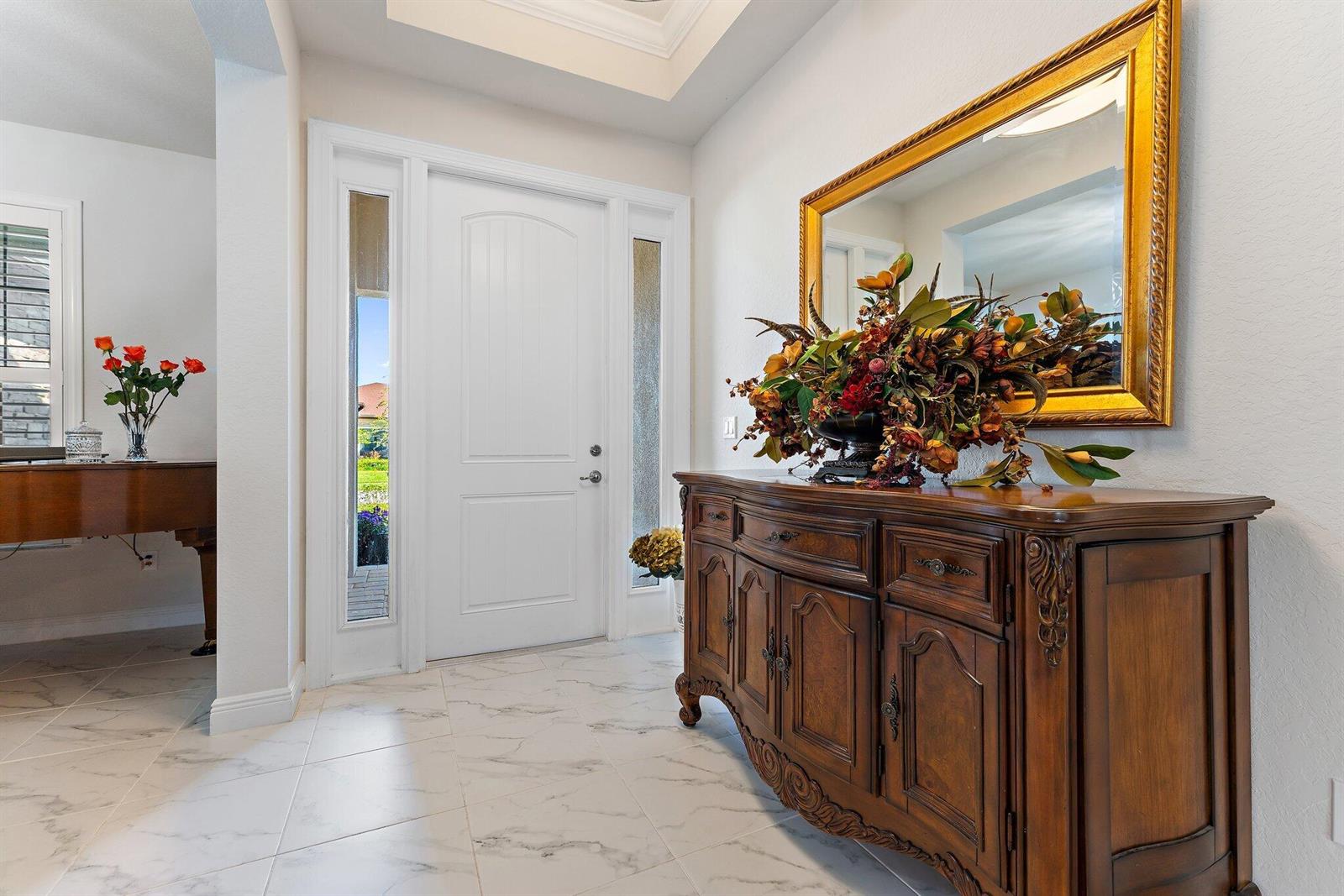 A foyer features white marble-look tile flooring, a wooden sideboard, and a gold-framed mirror — 6291 Arcadia Square, Vero Beach FL 32966, VERO BEACH, FL