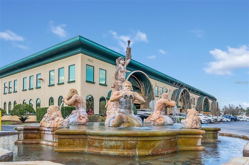 A large stone fountain with mythological figures sits in front of a modern commercial building — 6881 KINGSPOINTE PARKWAY UNIT 11, ORLANDO, FL