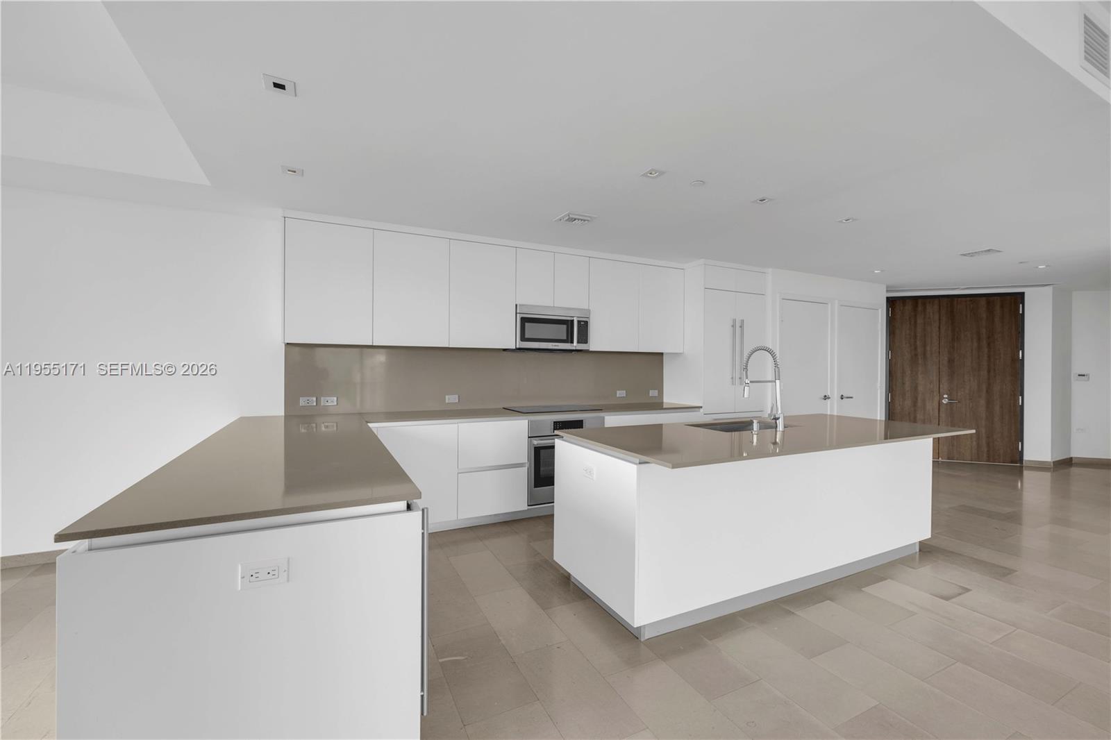 A modern kitchen features white cabinetry, a large island, and light-colored stone countertops — 88 SW 7th St # 3711, Miami FL 33130, MIAMI, FL