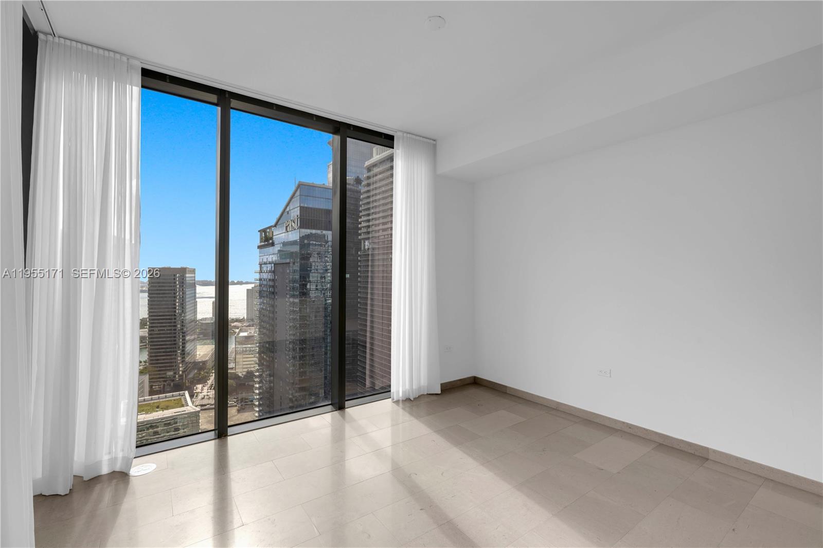 An empty room with floor-to-ceiling windows, light tile flooring, and a city skyline view — 88 SW 7th St # 3711, Miami FL 33130, MIAMI, FL