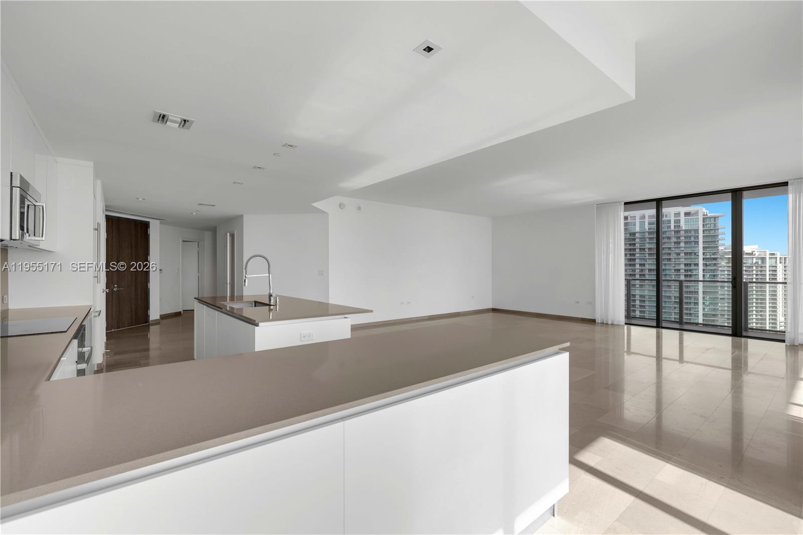 A modern kitchen with white cabinets and quartz countertops opens into a spacious living area — 88 SW 7th St # 3711, Miami FL 33130, MIAMI, FL