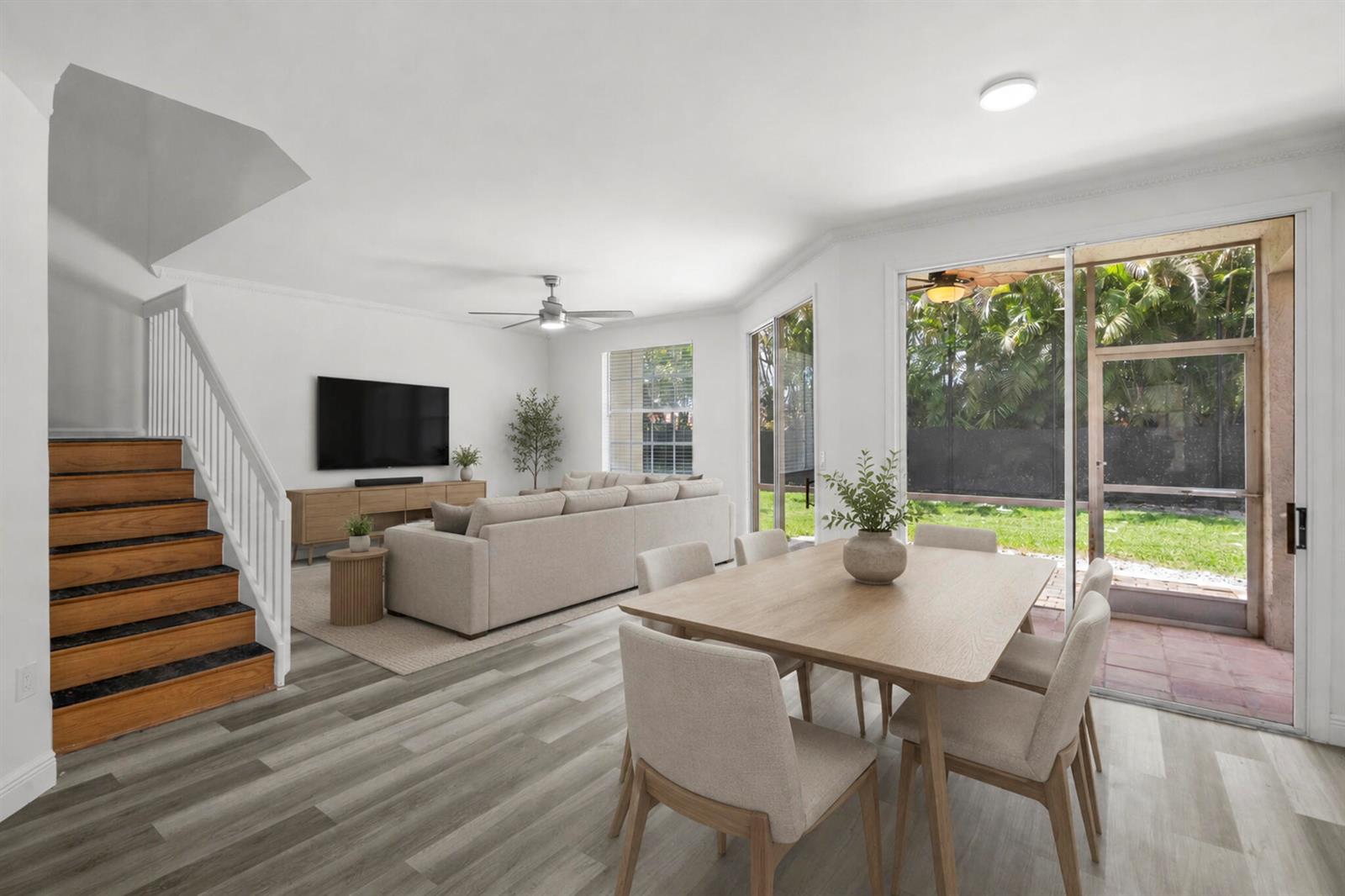An open-concept living and dining area features wood-look flooring, a staircase, and sliding glass doors — 20970 Via Oleander # D, Boca Raton FL 33428, BOCA RATON, FL