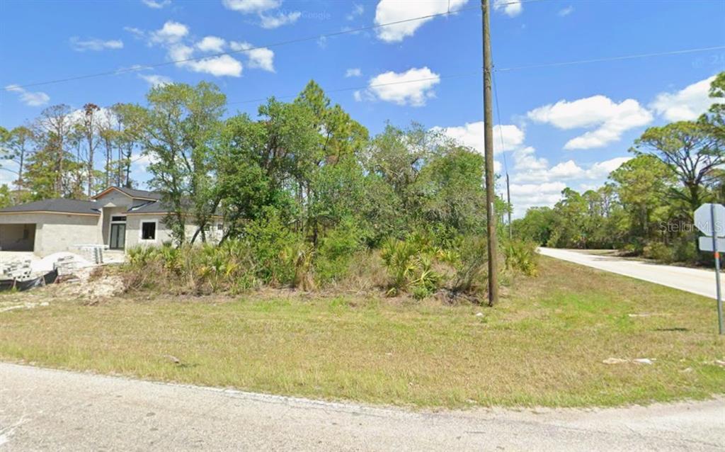 A vacant, wooded lot sits next to a house under construction near a paved road — 1087 JACOBS STREET, PORT CHARLOTTE, FL