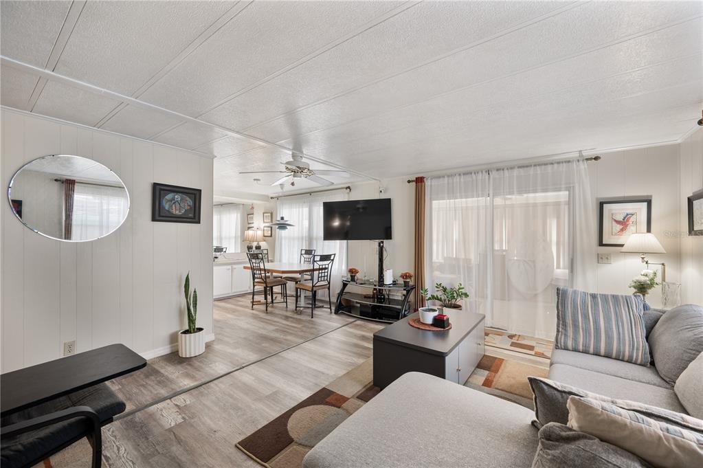 A living room with light wood-look flooring, a grey sectional sofa, and a dining area — 1610 REYNOLDS ROAD UNIT 126, LAKELAND, FL