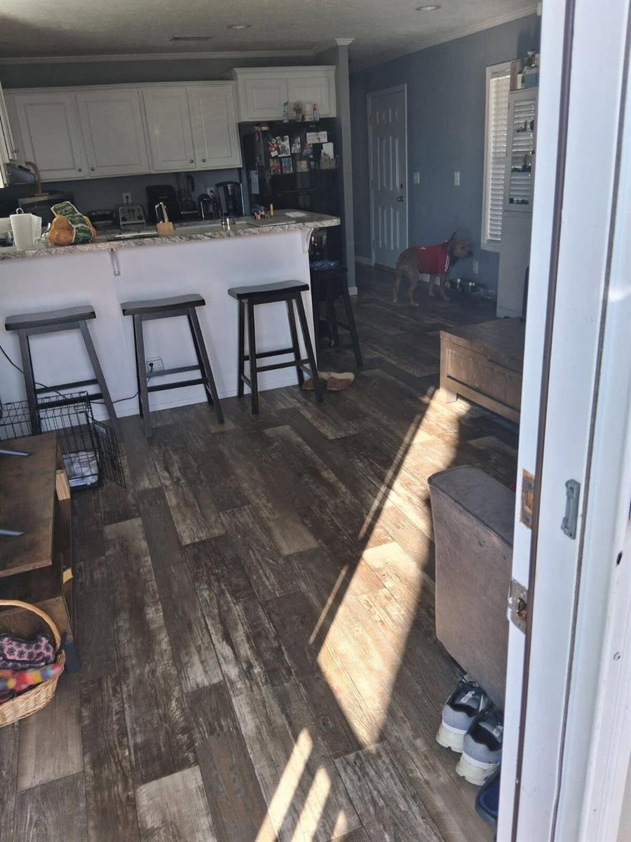 A kitchen with white cabinets and a breakfast bar overlooks a living area with wood-look flooring — 356 Mockingbird Avenue, Fort Pierce FL 34982, FORT PIERCE, FL