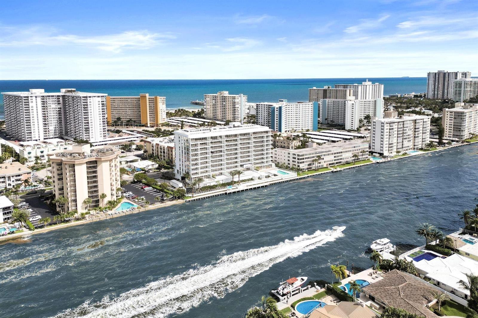 An aerial view shows a waterway with a boat and surrounding high-rise residential buildings — 407 N Riverside Drive # 204, Pompano Beach FL 33062, POMPANO BEACH, FL