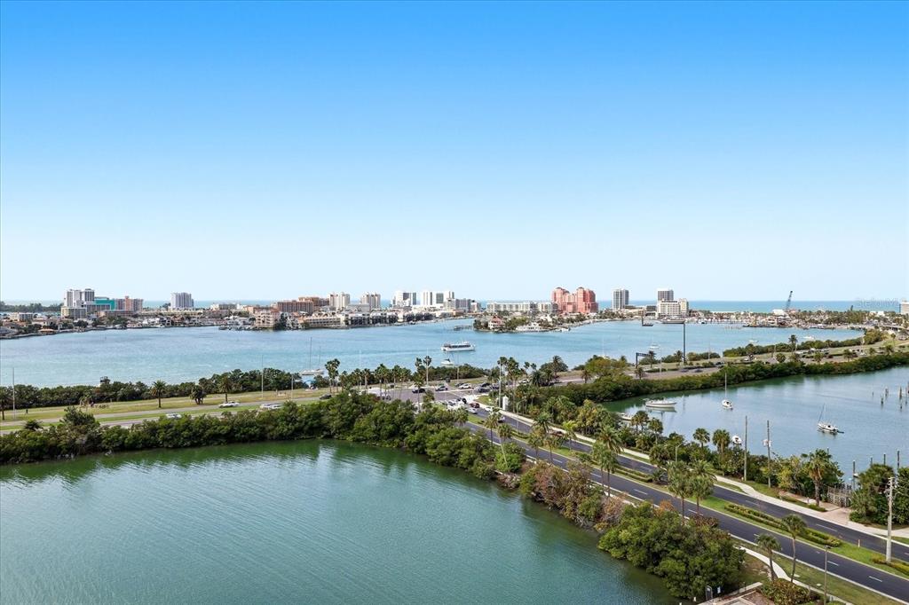 An elevated view of a coastal waterway with a road, palm trees, and distant buildings — 31 ISLAND WAY UNIT 1205, CLEARWATER BEACH, FL