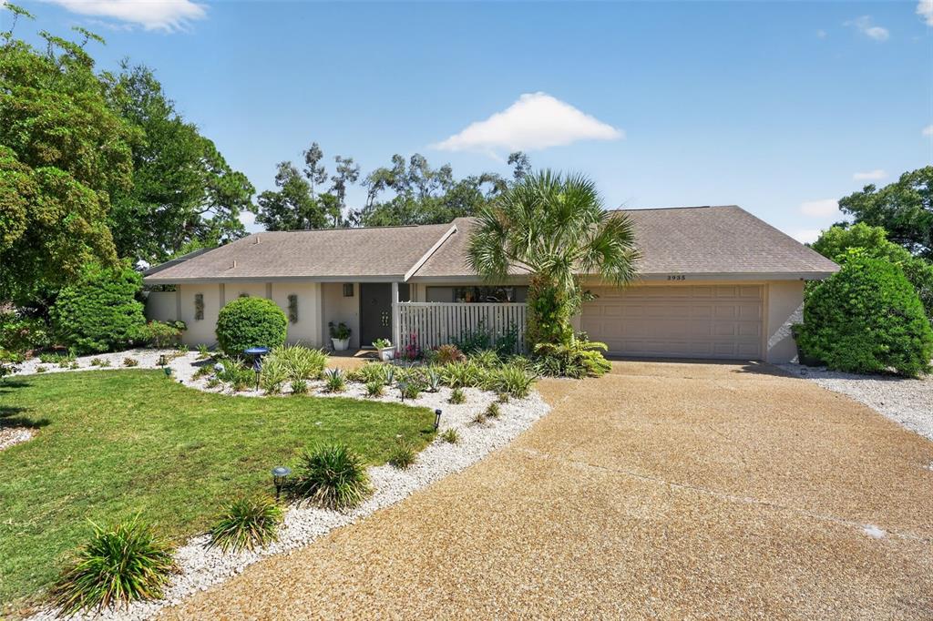 A single-story house with a beige exterior, a two-car garage, and a landscaped front yard — 3935 COUNTRY VIEW LANE, SARASOTA, FL