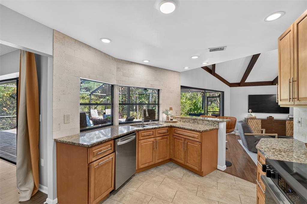 A kitchen with wood cabinets, granite countertops, and a tiled backsplash overlooks a living area — 3935 COUNTRY VIEW LANE, SARASOTA, FL