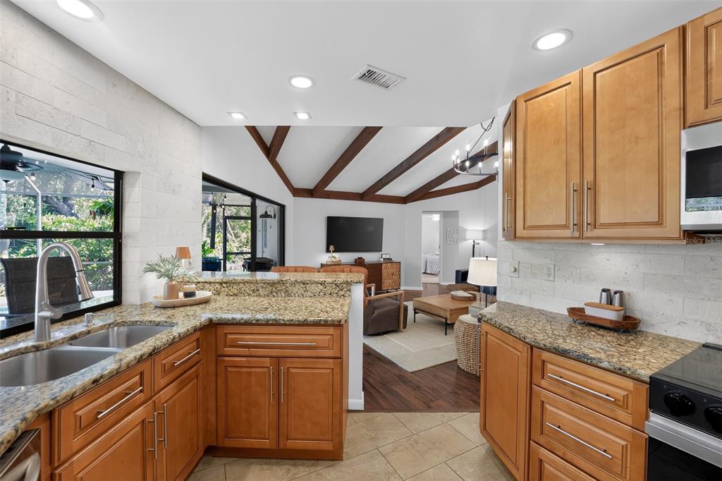 A kitchen with granite countertops and wood cabinets overlooks a living room with vaulted ceilings — 3935 COUNTRY VIEW LANE, SARASOTA, FL