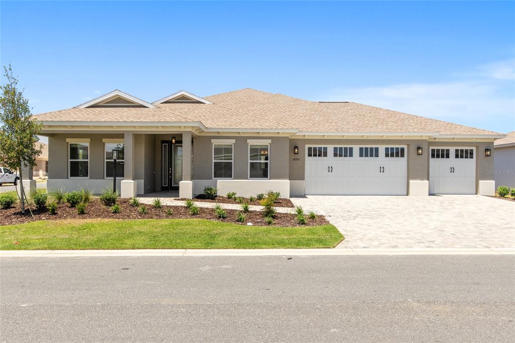 A single-story house with a beige stucco exterior, a shingled roof, and a three-car garage — 10261 SW 82ND PLACE ROAD, OCALA, FL
