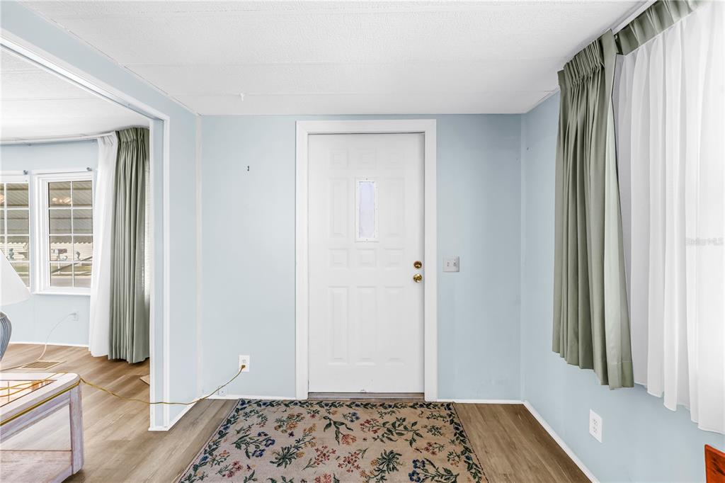 An interior view of a room with light blue walls, a white door, and wood flooring — 1100 BELCHER ROAD S UNIT 502, LARGO, FL