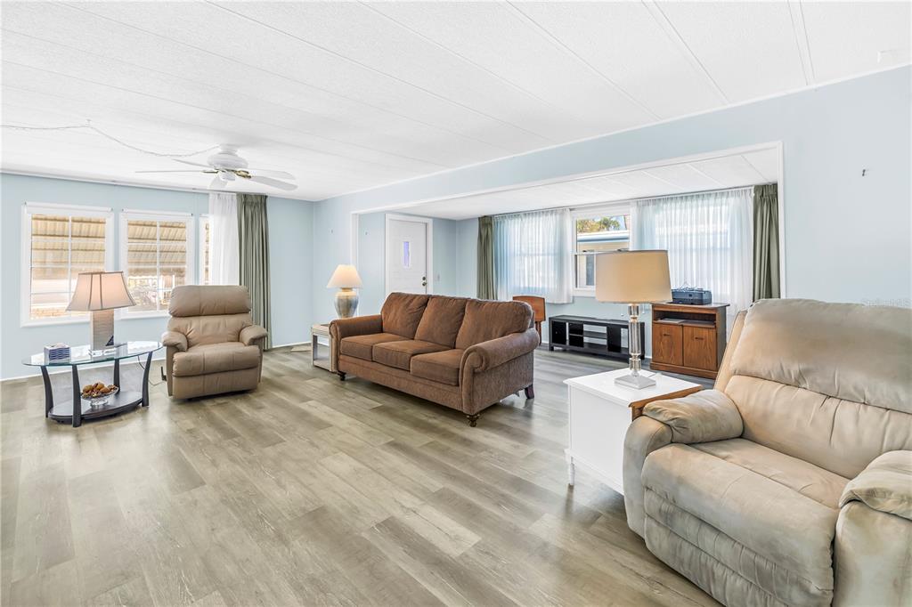 A living room with light blue walls, wood-look flooring, a brown sofa, and two recliners — 1100 BELCHER ROAD S UNIT 502, LARGO, FL
