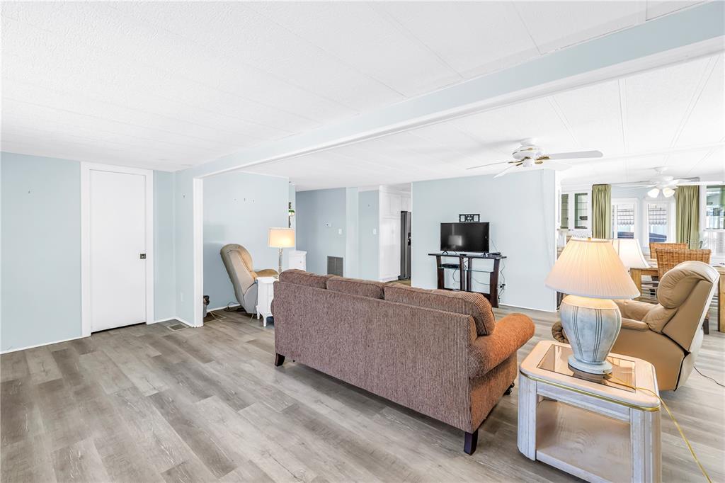 A living room with light blue walls, wood-look flooring, a brown sofa, and two recliners — 1100 BELCHER ROAD S UNIT 502, LARGO, FL
