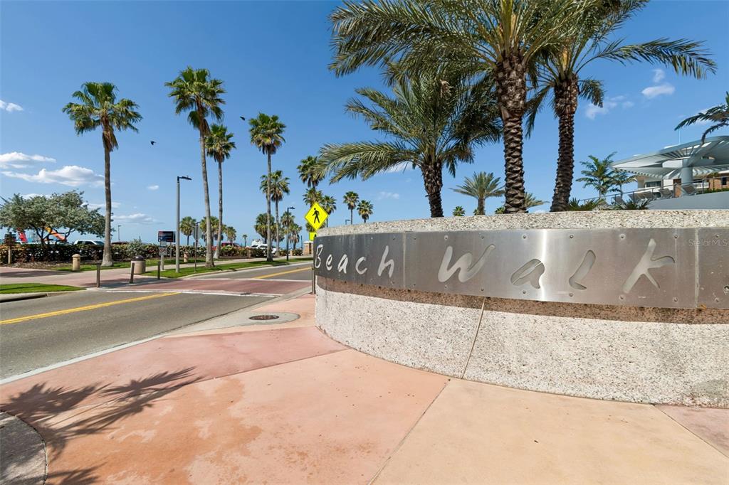 A curved stone wall with a metal Beach Walk sign stands beside a paved road — 400 CORONADO DRIVE, CLEARWATER BEACH, FL