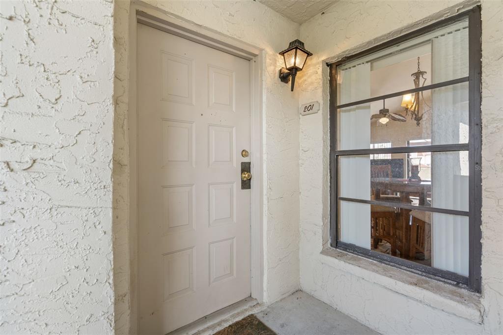 An exterior view of a white front door and a window showing an interior room — 2571 CYPRUS DRIVE UNIT 1-201, PALM HARBOR, FL