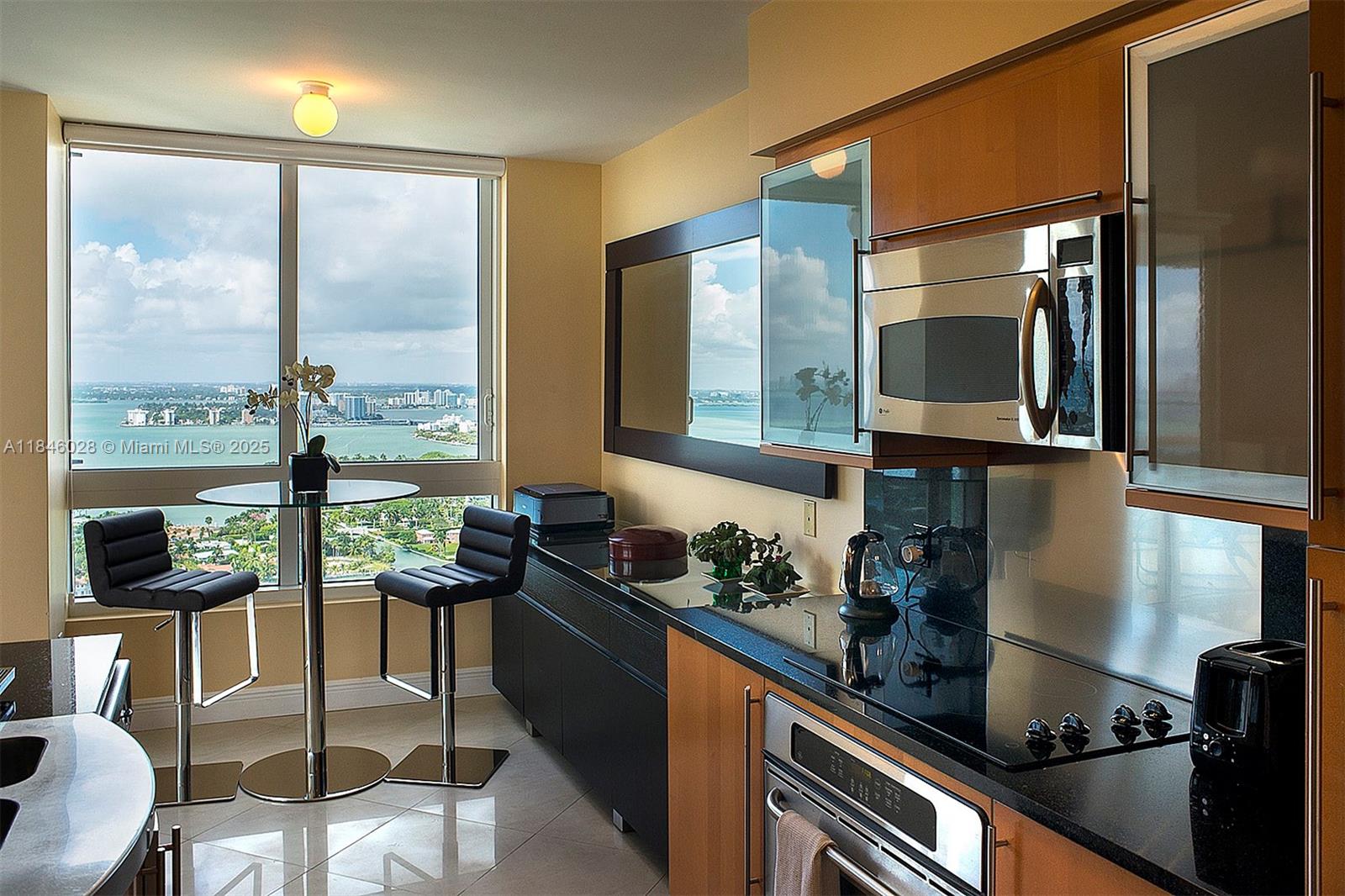 A modern kitchen features wood cabinets, black countertops, and a dining area with water views — 6365 Collins Ave # 3907, Miami Beach FL 33141, MIAMI BEACH, FL