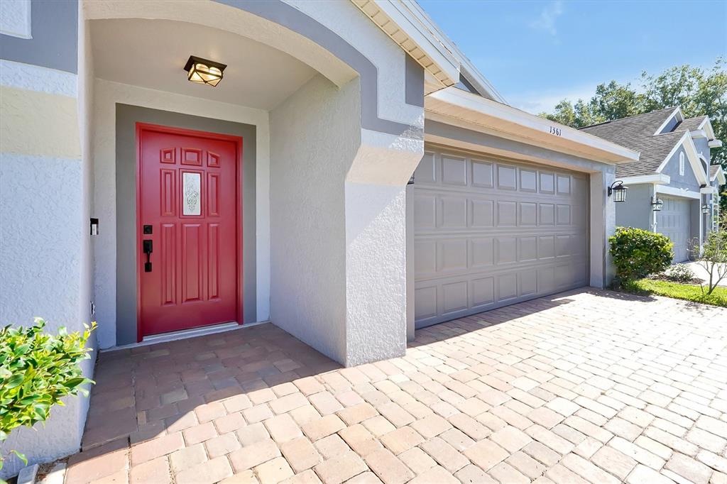 A red front door sits next to a gray garage on a paved driveway — 1361 HOLLY GLEN RUN, APOPKA, FL