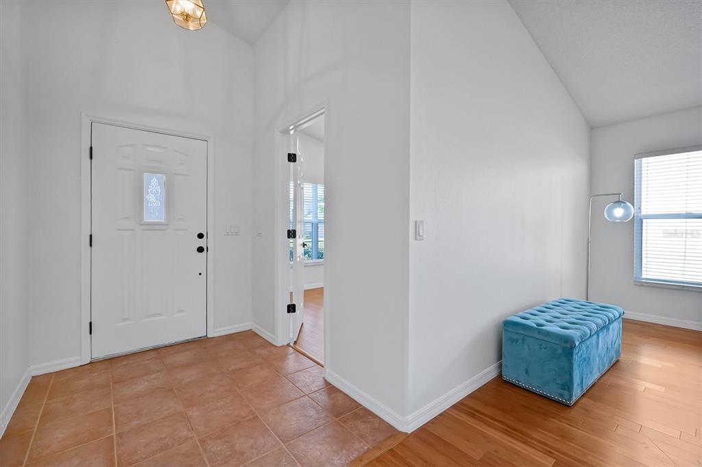 An entryway features tile flooring, a white front door, and a blue tufted storage ottoman — 1361 HOLLY GLEN RUN, APOPKA, FL